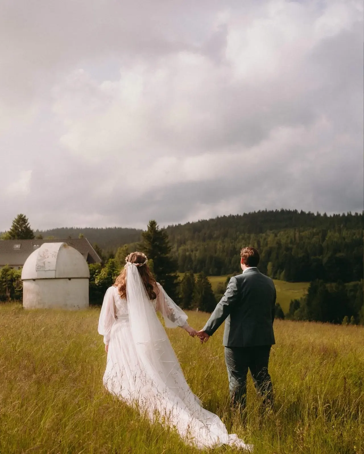 Brautpaar von hinten auf einer Wiese vor dem Nadelwald des Schwarzwalds