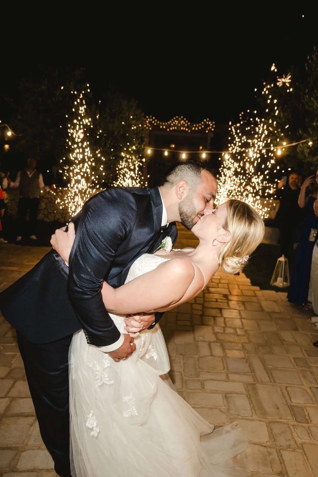 Bräutigam hebt Braut beim Kuss bei Nacht – Lichterketten und Feier-Atmosphäre